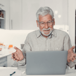 an older man, grey hair, sitting at desk with laptop, appears to be on zoom call