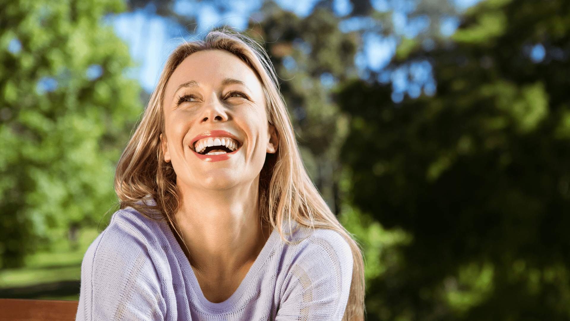 A woman sitting on a park bench, smiling and looking up