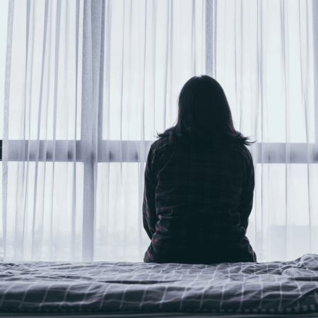 Back of a woman, sitting on abed, looking out of the window
