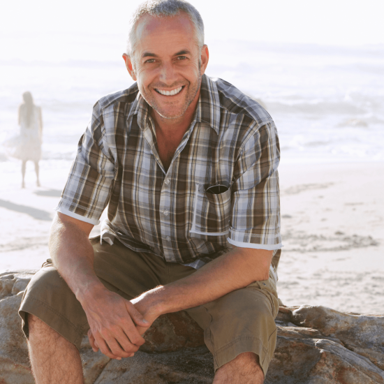man sitting on rocks at beach, smiling