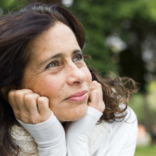 A woman sitting in a park, head resting on hands, contemplating